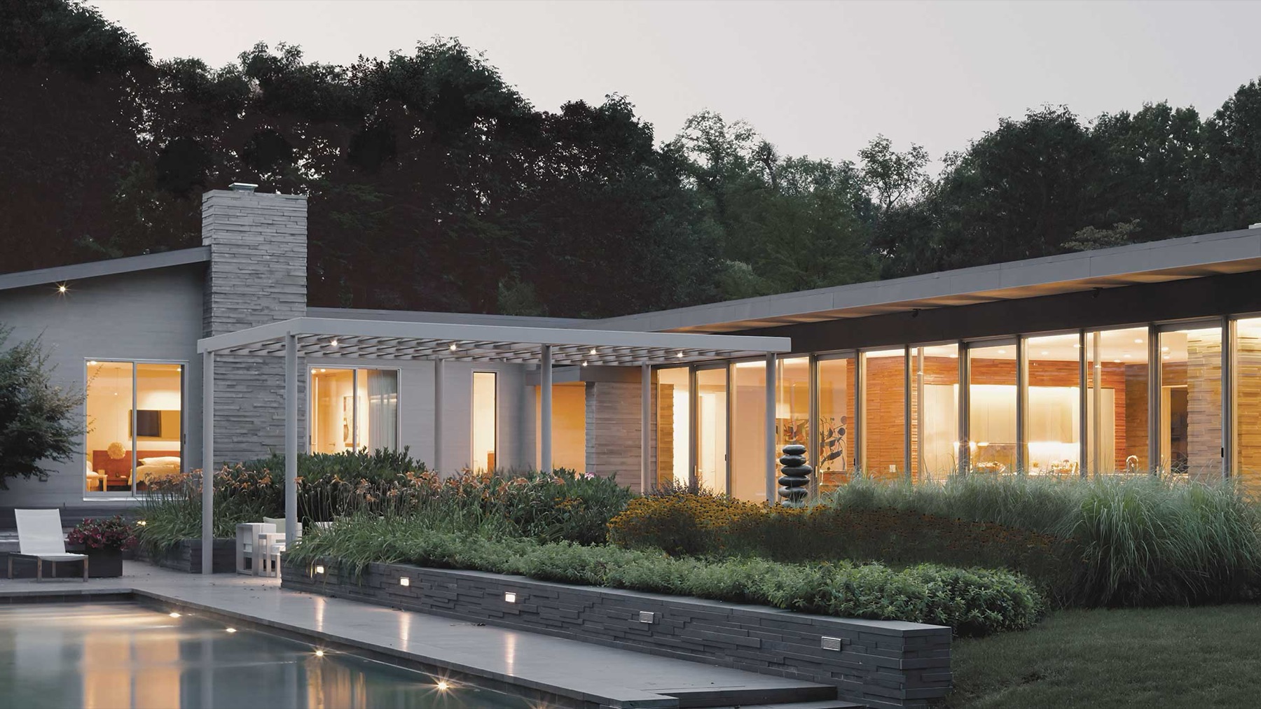 A modern home at dusk with warm interior lighting and lit landscape